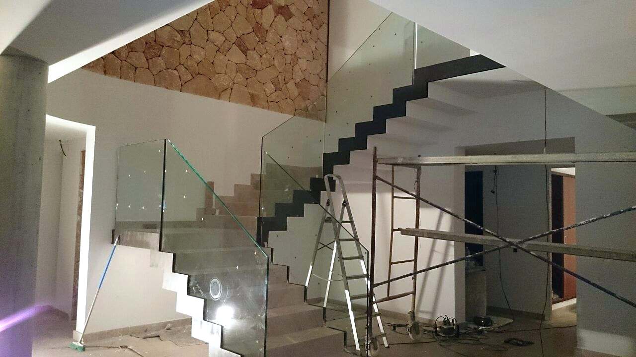 Escalera volada en un espacio de doble altura con barandilla de vidrio, aún en obra