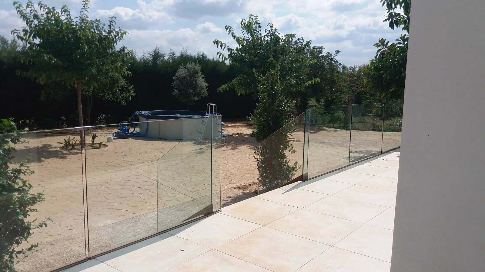 Terraza con barandilla de vidrio continua que da a un jardín con árboles