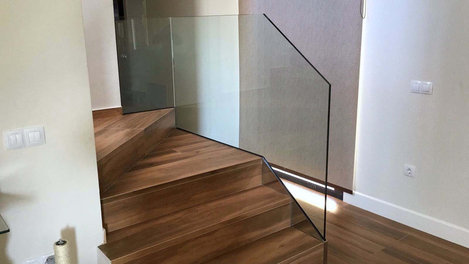 Escalera de madera con barandilla de vidrio que acompaña el giro del rellano
