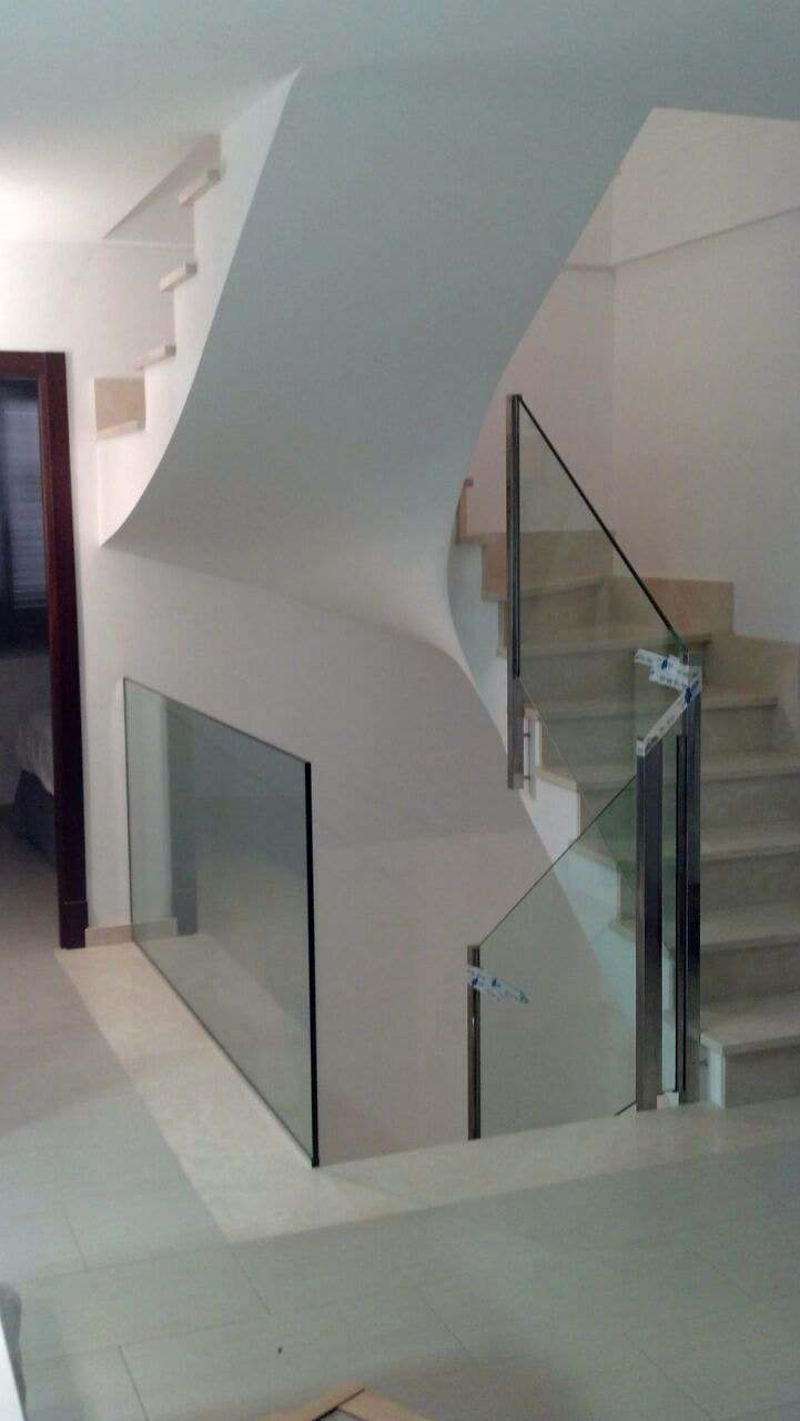 Escalera curva blanca con barandilla de vidrio y pasamanos de acero inoxidable