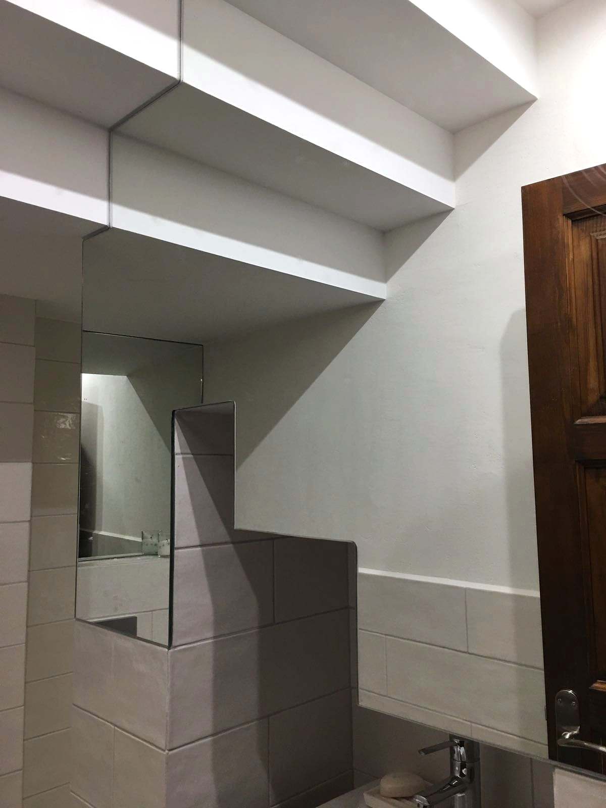 Espejo recortado que encaja entre volúmenes y escalones de una pared