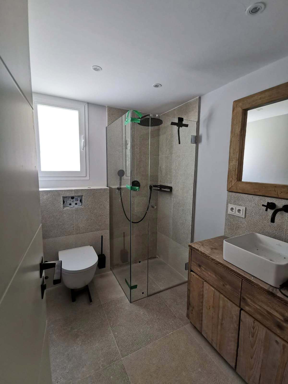 Baño con mueble de madera y mampara angular de vidrio junto a la ventana