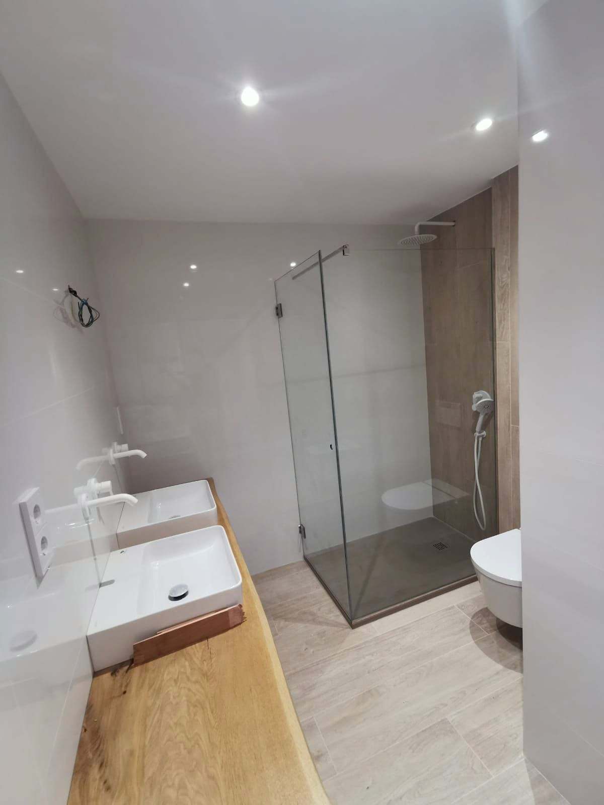 Baño luminoso con plato de ducha cerrado por un fijo de vidrio y puerta batiente