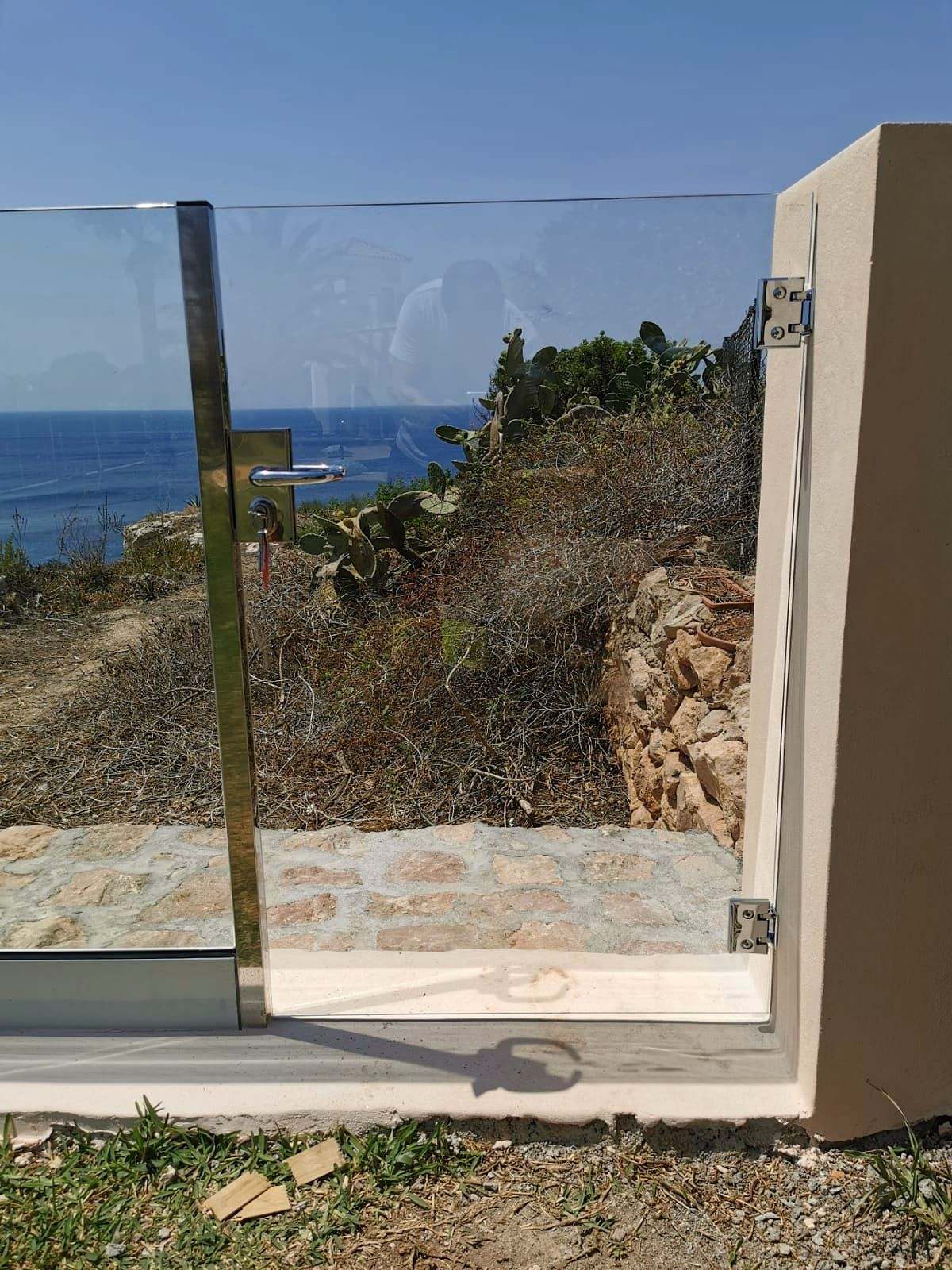 Puerta de vidrio templado con cerradura que da paso a un sendero junto al mar