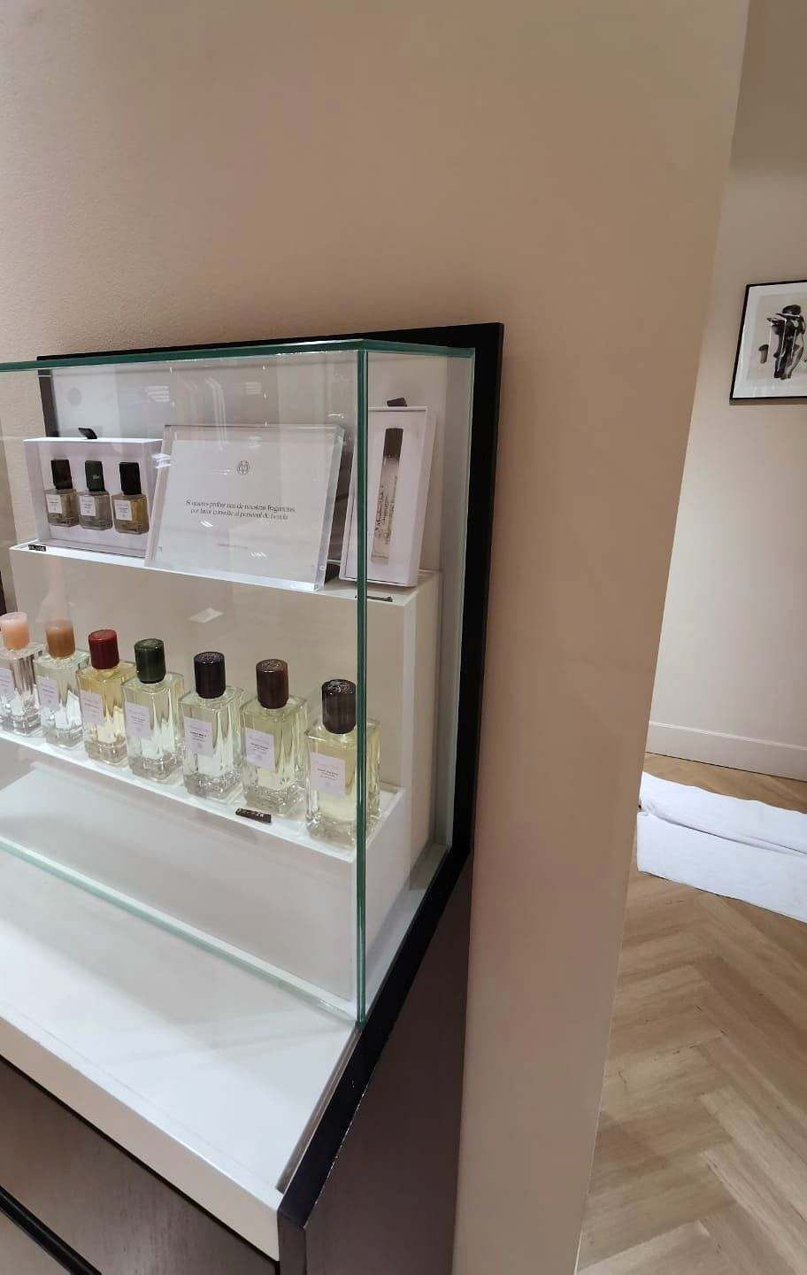 Urna de cristal sin perfiles sobre una peana negra, con frascos de perfume dentro